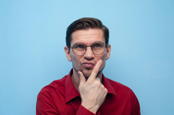 Portrait of a pensive serious young man in a shirt and glasses on a blue background. - Valokuva, kuva