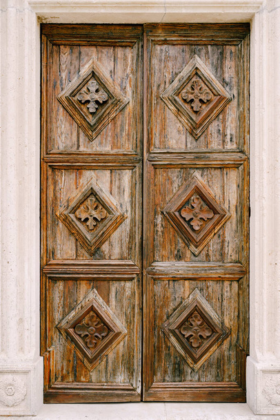 Drewniane brązowe drzwi z rzeźbionymi diamentami i wzorami w otworze białej ściany. - Zdjęcie, obraz
