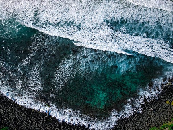 Fotografía aérea de alta definición de las olas oceánicas en una costa rocosa con árboles de selva verde en el fondo. Frío Invierno Azul Verde Agua y Piedra Playa con Rompiendo Surf - Foto, Imagen