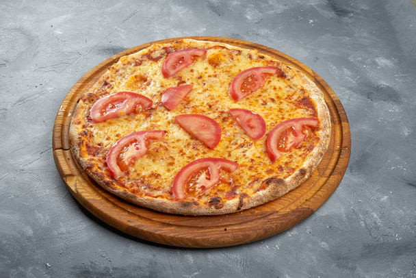Baked italian pizza with tomatoes and cheese on a wooden tray on a gray background - Valokuva, kuva