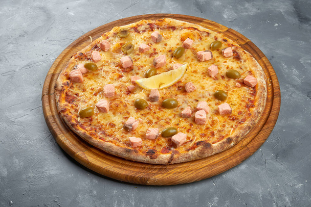 Baked italian pizza with salmon, olives and cheese on a wooden tray on a gray background. - Valokuva, kuva