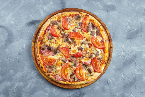 Baked italian pizza with tomatoes, bacon, beef and cheese on a wooden tray on a gray background. - Foto, immagini