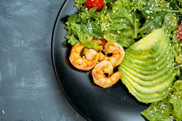 Salad with shrimps, avocado and cherry tomatoes in a black plate on a gray background. Top view. Half of plate - Foto, afbeelding