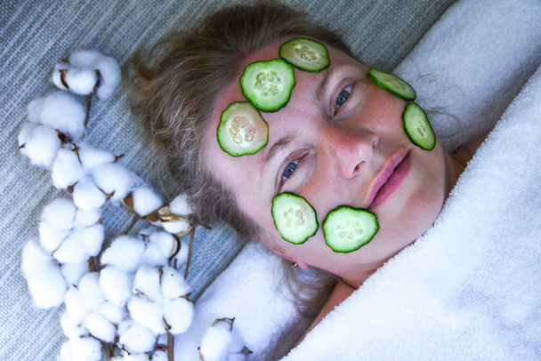 Caucasian woman mask cosmetic mask and cucumber patches face for beauties at home. Female lying on couch home and doing restoring face masks portrait. Healthy facial skin care at home help concept. Woman applying homemade facial mask - Photo, Image