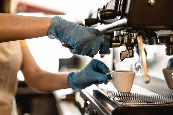 Young woman making coffee espresso while wearing surgical mask and gloves for preventing corona virus spread - Bar owner safety working - Hot beverages and covid-19 rules concept - Zdjęcie, obraz