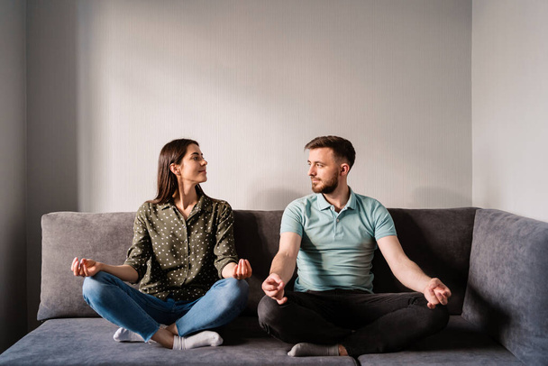 Man and woman sitting on sofa in lotus pose - Photo, Image