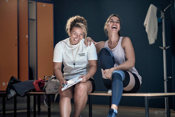 Female personal trainer and her client have good fun in a locker room before training - Foto, Bild