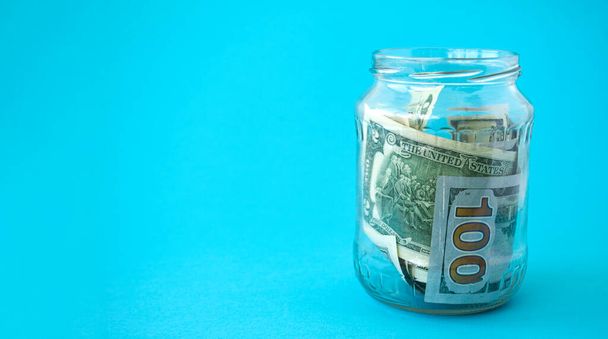 Piggy bank from a glass jar with new dollars for life on a blue background. Copy space. Economy concept. - Photo, Image