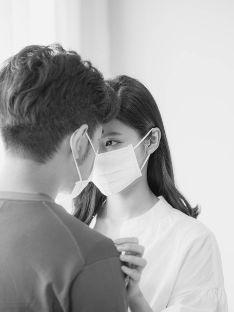 Νεαρή Ασιάτισσα και άνδρας φορώντας χειρουργική μάσκα στο σπίτι σε μαύρο και άσπρο - Φωτογραφία, εικόνα