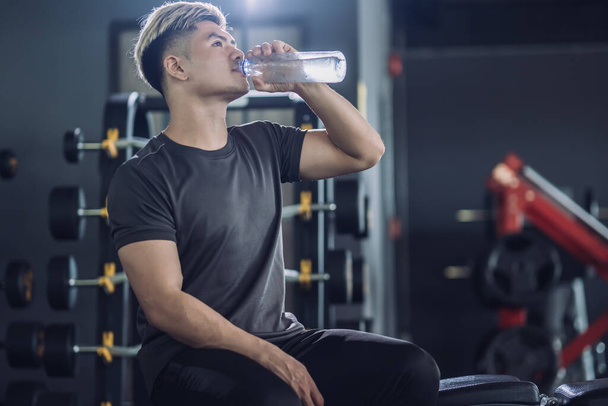 Sportsman in t-shirt drinking water in the fitness gym, Handsome sporty resting, having break after doing exercise. Attractive athletic man after training workout relax concept. - Foto, immagini