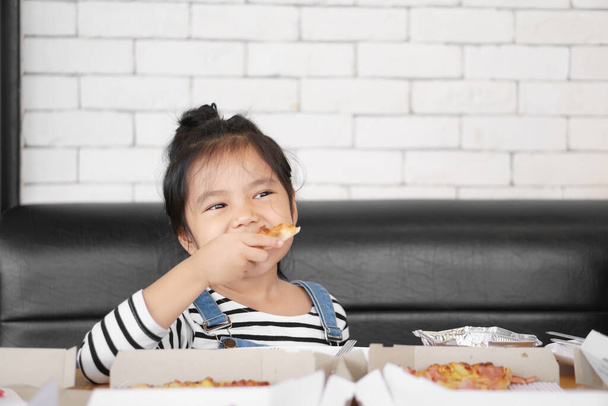 Niño asiático linda o niña disfrutar de comer pizza hawaiana o comida italiana en caja con queso grueso y crujiente delgada a hambre de desayuno feliz o almuerzo en el restaurante cafetería o en casa en la mesa y el sofá - Foto, Imagen