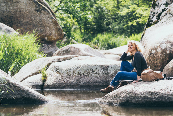 川の渓谷でハイキング中に休息をしているバックパックを持つ女性。ノルディックウォーキングポールとエコツーリズム - 写真・画像