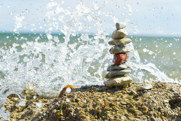 波が砕ける岩のビーチの石の塔。ソフトフォーカス楕円形小石同士が. - 写真・画像