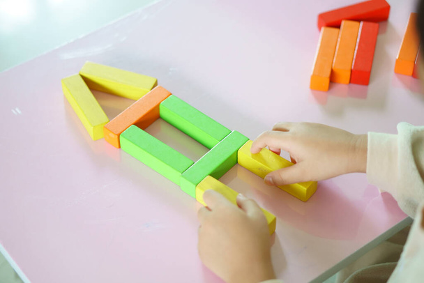 dětská ruka nebo dítě myšlení hrát barevné dřevo blok hračka pro učení vzdělávání na stavbu domu nebo rodinného domu a financovat investice nebo budoucí rozvoj peněz s nemovitostmi ve školce - Fotografie, Obrázek