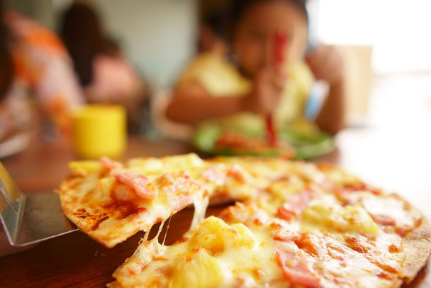 recogiendo pizza hawaiana delgada crujiente con queso elástico y jamón con piña en bandeja o plato para el almuerzo o el desayuno y la cena con la familia y comer deliciosa comida en la mesa en el restaurante italiano - Foto, Imagen