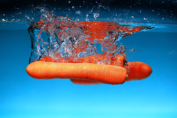 Carrot in the water splash over blue - Foto, afbeelding