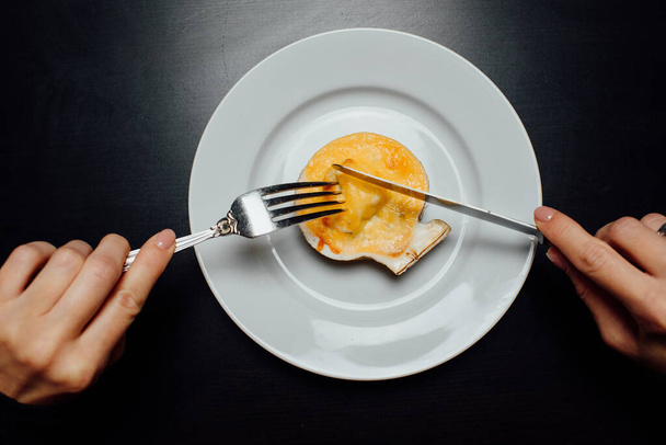 baked scallops in a shell with cheese on a white plate with a knife and fork on a black background - Photo, Image