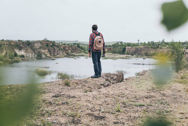 Muž s batohem na horách. Stojící na okraji útesu a s výhledem na skalnatý kaňon - Fotografie, Obrázek