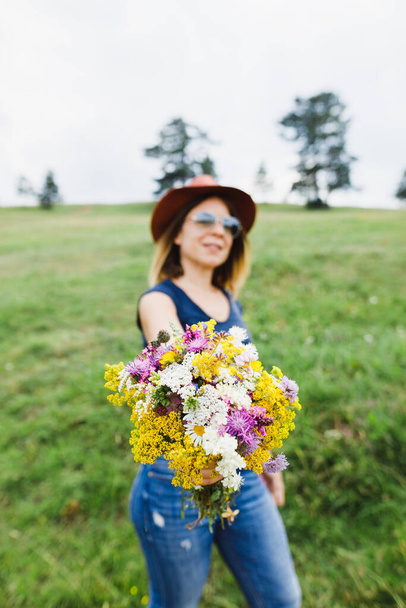 Mujer joven sosteniendo ramo de flores en el campo - Foto, imagen