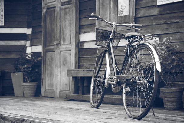 старый велосипед или велосипед перед ретро деревянной домашней террасой с деревянной дверью и окном между деревом в цветочном горшке для внешнего и внутреннего декора или классический фон на винтажном голубом и белом - Фото, изображение