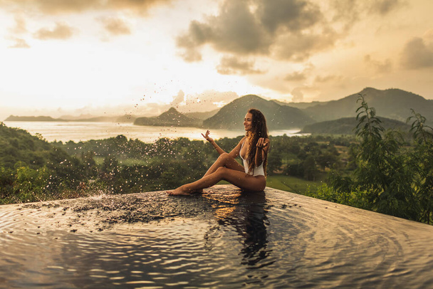 Dream journey in Asia. Woman sitting on edge luxury infinity pool an enjoying amazing mountain, rice terraces and coastline view at sunset. Inspiration travel destination. - Photo, Image