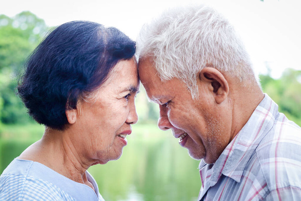 Ασιατικά ζευγάρια που έχουν ζήσει μαζί για πάνω από 50 χρόνια, βάζουν τα μέτωπά τους κοντά, χαμογελώντας και ευτυχισμένα. Να προσέχετε ο ένας τον άλλον για μια ζωή. Έννοια ανώτερης κοινότητας - Φωτογραφία, εικόνα