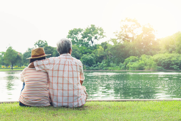 An elderly couple hugging each other with love and happiness in a park with a large pond. Senior community concept, good health, longevity - Photo, Image