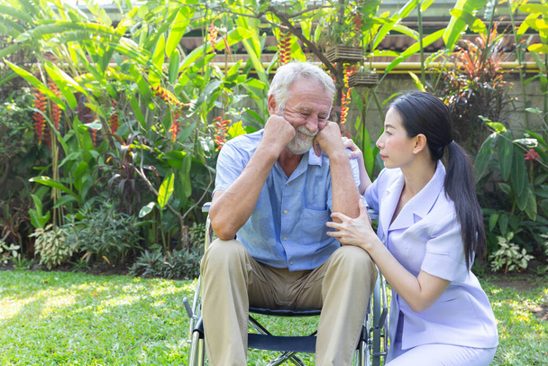 Nurse take care a depressed thoughtful senior retirement man on his wheelchair in a garden in his home - Photo, Image