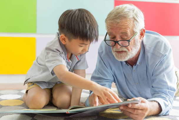 Großvater und kleiner süßer Enkel lesen gemeinsam Buch auf dem Fußboden in ihrem Haus - Foto, Bild