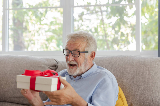 Senior retraite homme est heureux avec son cadeau d'anniversaire surprise sur le canapé dans sa maison - Photo, image
