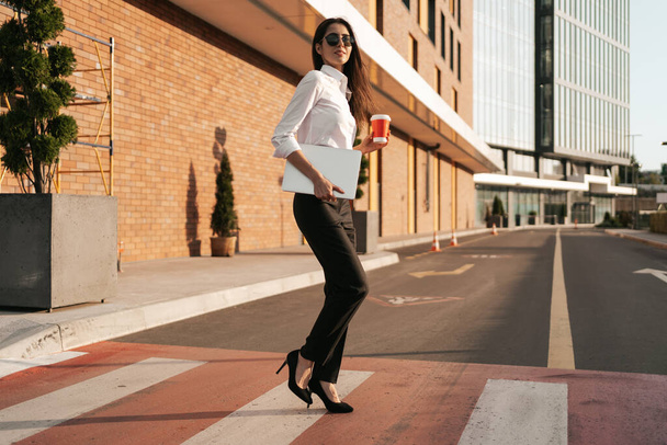 Жінка в білій сорочці тримає каву, щоб перейти вулицю
 - Фото, зображення