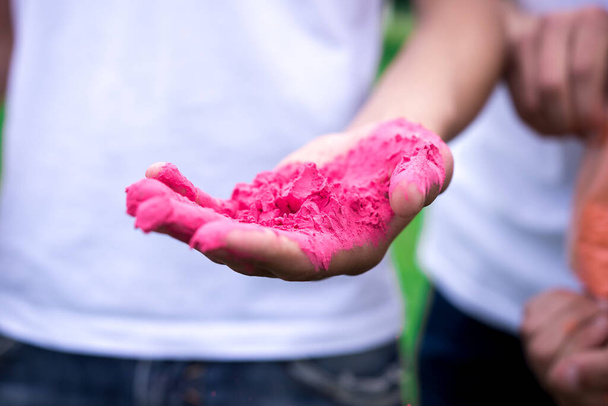 手をクローズアップで伝統的なホリ祭りのための色のピンクの粉。背景に白いTシャツを着た男が. - 写真・画像
