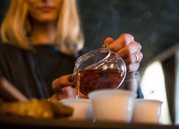 Tradiční čínský čajový obřad. Černý nebo červený čaj nalévání blondýny caicasian dívka do bílého pial pohár na tmavém pozadí stolu - Fotografie, Obrázek