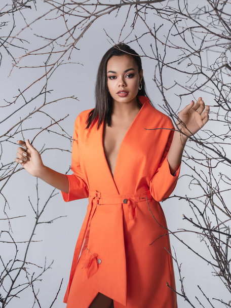 Beauty photo of young elegant african american woman.Looking at camera. Glamour makeup. Studio shot.Skin care and beauty concept.Studio shot.Happy beautiful african american woman posing in fashionable orange coat, standing on gray background - Фото, зображення