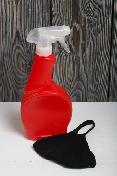 Red plastic bottle with spray. Cleaning spray. Face mask to protect against the virus. The mask is black. - Фото, зображення
