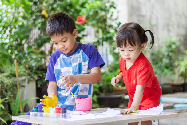Ázsiai testvérgyerekek rajzolnak és festenek színeket a szobában lévő papírra. Otthoni tanulás, társadalmi távolság. Gyerekek és oktatás koncepciója. - Fotó, kép