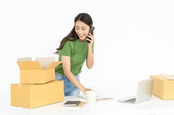 Portrait of a pretty Asian young girl working small business talk on smartphone while check order and packing product to box in home office.Startup Small business owner, SME, Delivery Concept. - Photo, Image