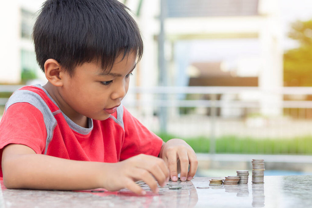 幸せなアジアの子供の少年の肖像画は、コインを数える。子供の頃はお金をテーブルの上に置いた。子供は将来の概念のためにお金を節約する。子供たちが学ぶ. - 写真・画像