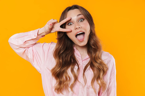 Image of beautiful excited woman gesturing peace sign on camera isolated over yellow background - Zdjęcie, obraz