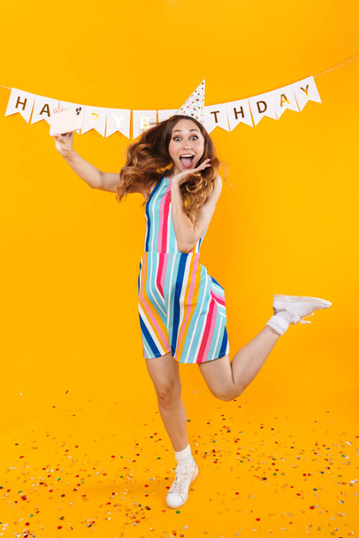 Image of excited cute woman taking selfie on mobile phone and dancing isolated over yellow background - Foto, Imagem
