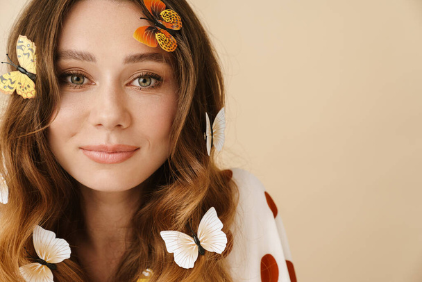 Photo of beautiful pleased woman with fake butterflies posing and looking at camera isolated over beige wall - Foto, Imagem