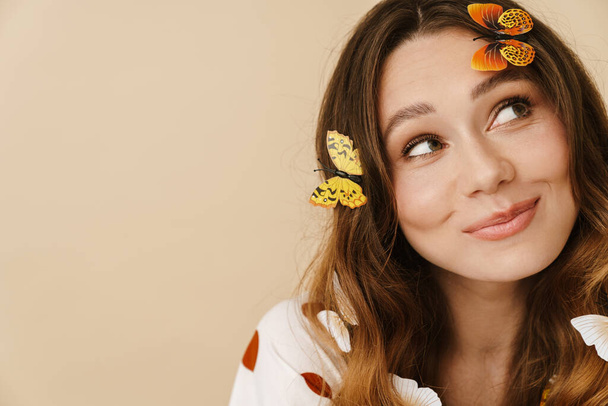 Photo of attractive joyful woman with fake butterflies smiling and looking aside isolated over beige wall - Foto, imagen