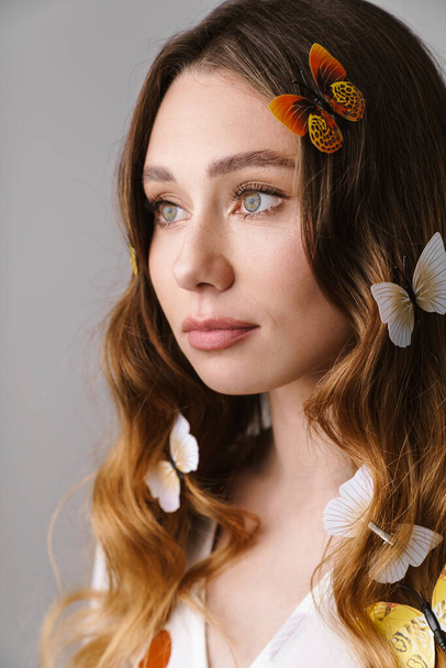 Photo of beautiful caucasian woman with fake butterflies posing and looking aside isolated over gray wall - Foto, Imagen