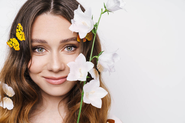 Photo of cheerful woman with fake butterflies and flower smiling at camera isolated over white wall - Photo, Image