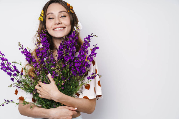 Photo of cheerful woman with fake butterflies and flowers smiling at camera isolated over white wall - Foto, afbeelding