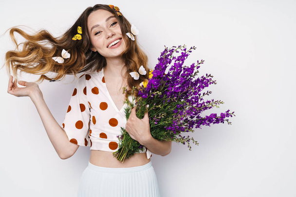 Photo of cheerful woman with fake butterflies and flowers smiling at camera isolated over white wall - Foto, Imagen