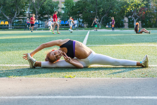 Teenage girl is training at the stadium, doing stretching on the twine. A teenage girl is warming up before running in the stadium - Photo, Image
