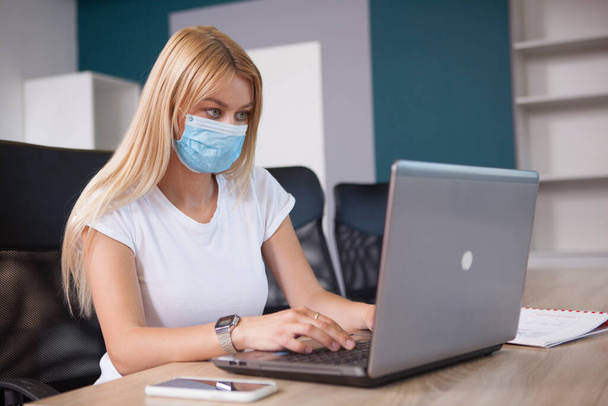 Bionda donna d'affari dai capelli concentrandosi, lavorando sul suo computer portatile, indossando maschera facciale durante la pandemia covid - Foto, immagini