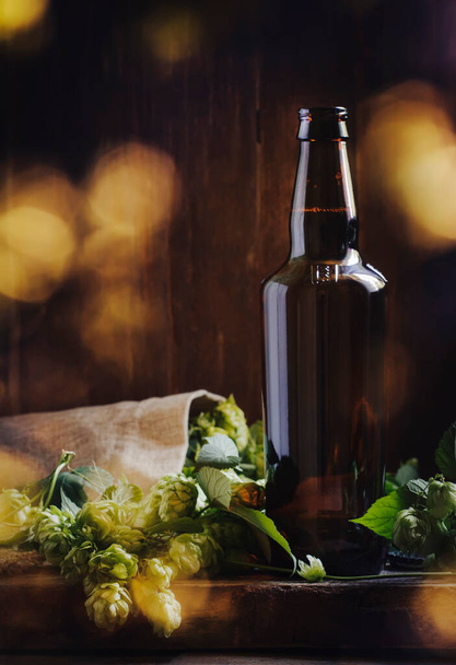 Dark beer bottle, ale or stout iin big glass with hop cones, wooden bar counter - Φωτογραφία, εικόνα