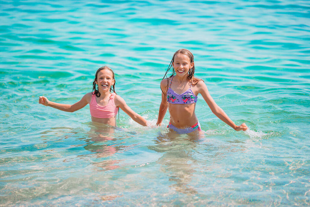 Happy children splashing in the waves during summer vacation on tropical beach. Girls play at the sea. - Photo, Image